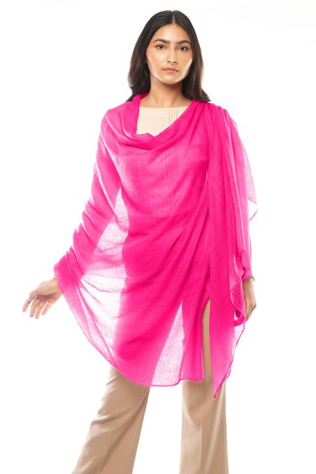 A woman wraps a bright pink cashmere scarf around her body, showcasing its generous size and lightweight silhouette. She wears cream-colored top and beige high-waisted trousers, letting the scarf’s vibrant hue radiate timeless beauty.