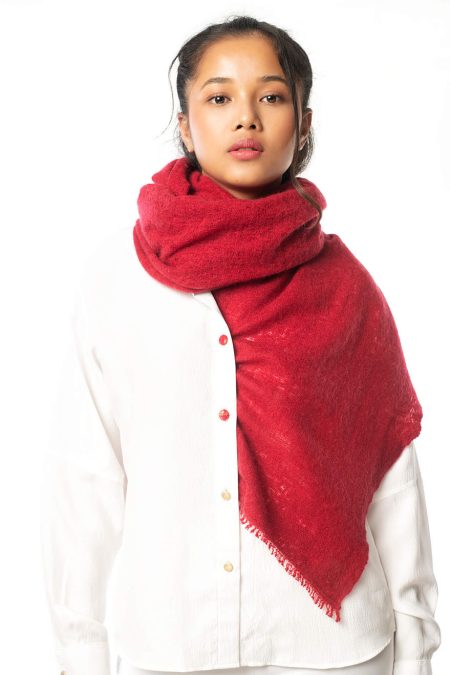 Model wearing a red hand-knitted cashmere scarf wrapped around her neck, with one end elegantly tucked into her white shirt. The scarf’s luxurious texture and elegant style are highlighted against the model's outfit.