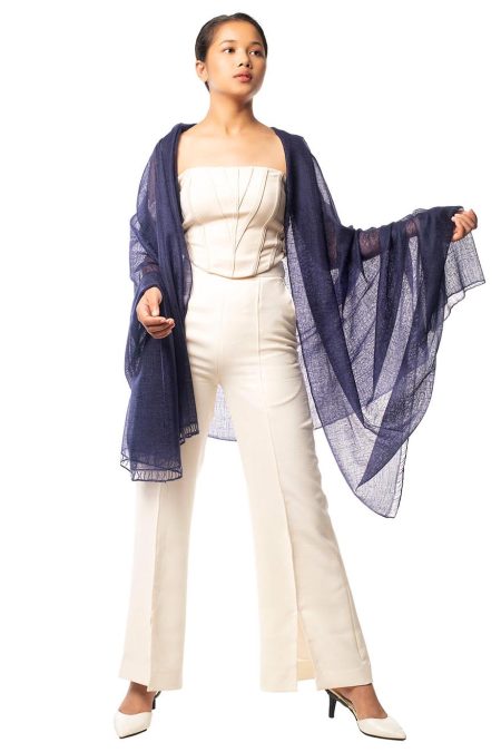 Full-body view of a woman draped in an indigo blue cashmere scarf, paired with a cream corset top and matching pants.