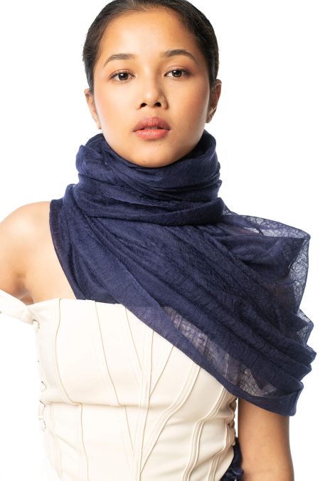 A woman wearing an indigo blue cashmere scarf wrapped around her neck styled elegantly with a cream corset top.