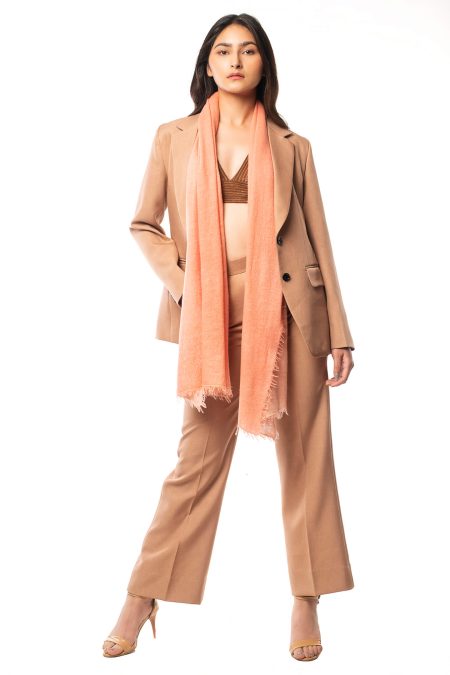 Model styled in a light salmon pink cashmere scarf, draped casually around the neck, emphasizing the versatility and luxurious feel of hand-knitted 100% cashmere.