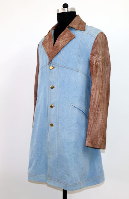 A mannequin displaying men's handmade light blue denim hybrid coat in a 3/4 length with hand-distressed leather sleeves, lapels, and the collar; profile view.