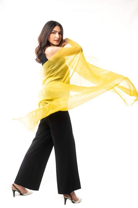 A woman in black pants and a vest posing with a yellow cashmere scarf stylishly wrapped around her body.