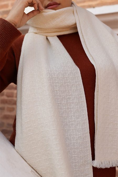 Close-up showing the detailed texture of an off-white pearl weave cashmere scarf worn around the neck over a rust-colored knit sweater.