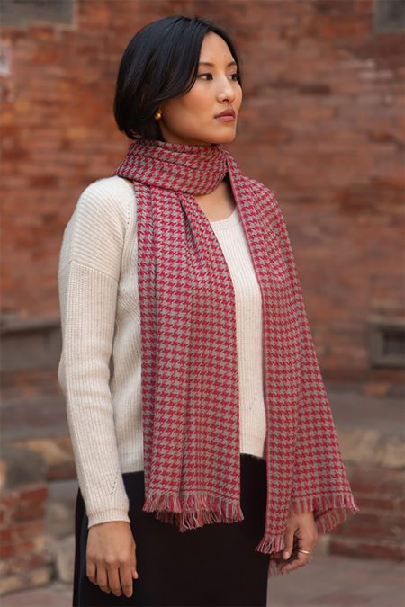 Red houndstooth cashmere scarf styled on a model, flowing naturally to highlight its pattern weave and vibrant crimson tones.