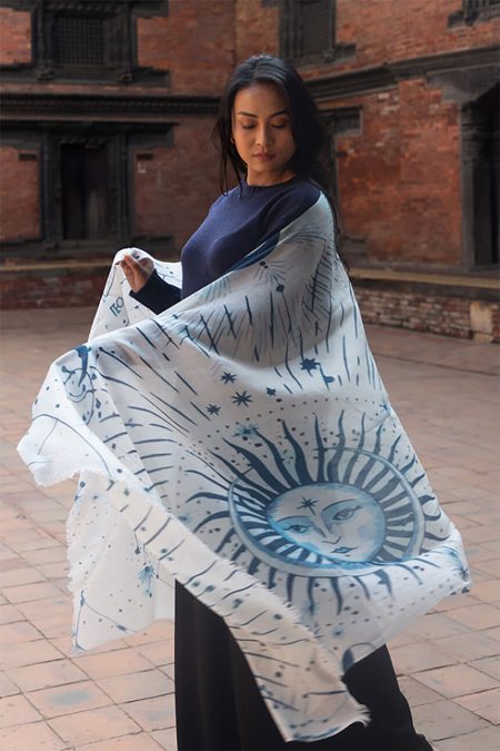 Woman looking down while the flowing Solar and Lunar Print Cashmere Scarf billows, highlighting the detailed sun face illustration.