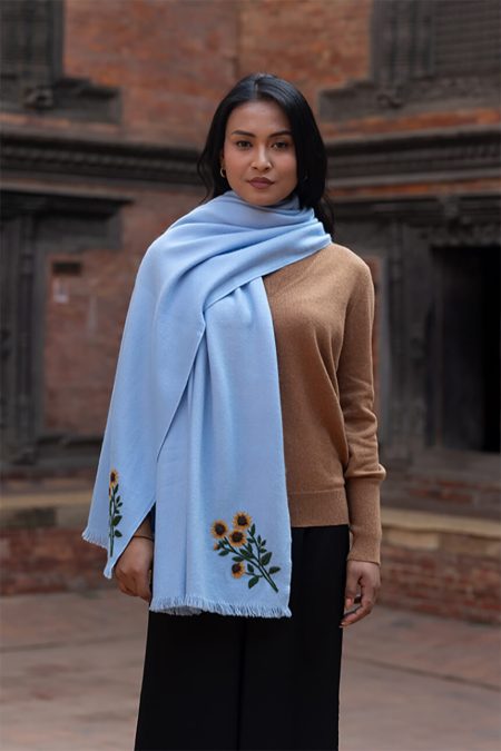 Medium portrait of a woman wearing the sunflower embroidered baby blue cashmere scarf against a backdrop of traditional architecture.