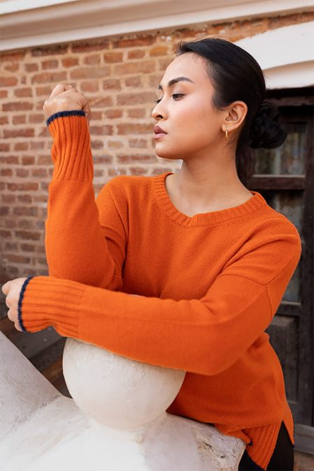 Woman in profile wearing Baron Boutique's Ember Glow orange cashmere dropped shoulder boxy sweater, displaying the sweater's relaxed drape, contemporary fit, dropped shoulder design, and soft cashmere texture.