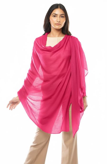 A woman models a hot pink featherlight cashmere scarf over a light top and khaki pants. The scarf is draped elegantly around her, creating a stylish, flowing silhouette.