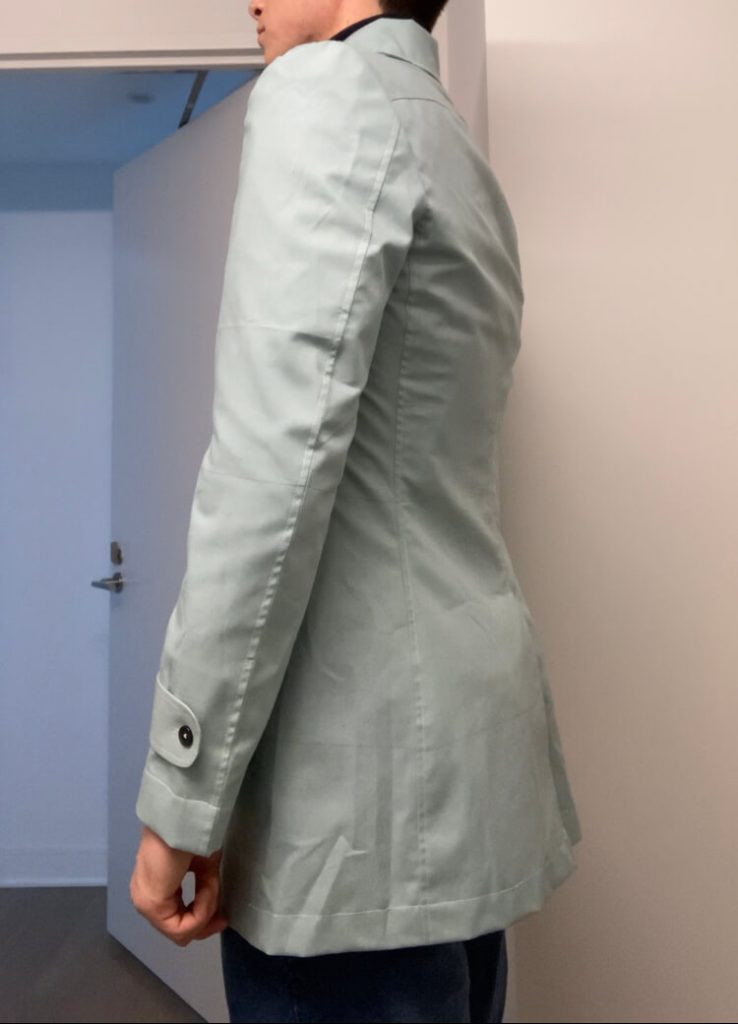 Side profile of bespoke car coat fitting canvas showing tailored silhouette and length customization during toile fitting.
