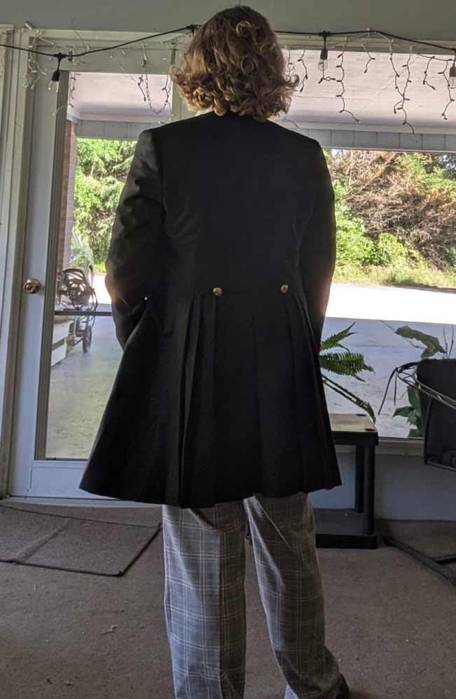 Customer wearing a custom-made 12th Doctor grey linen coat by Baron Boutique, showcasing the back view with pleated skirt details and button accents in profile.