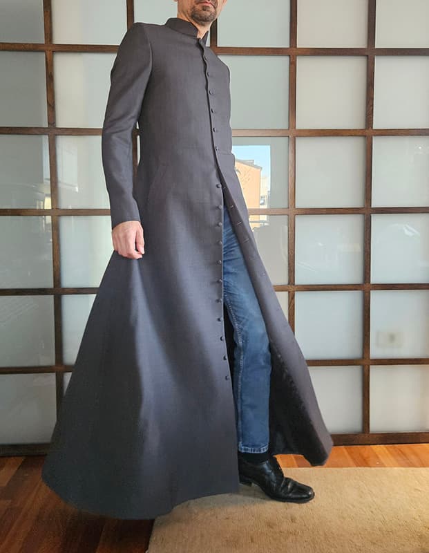 Happy customer wearing a bespoke Matrix Reloaded Neo coat inspired by Keanu Reeves’ iconic film costume. The tailored black full-length coat features a high Mandarin collar, concealed front closure, structured silhouette, and dramatic flowing hem, recreated with screen-accurate craftsmanship for a custom fit.