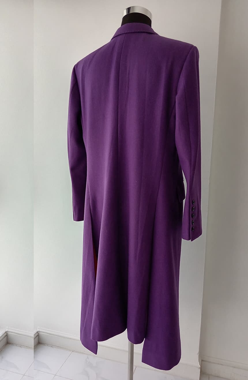 Back profile view of a Heath Ledger Joker inspired purple long coat from The Dark Knight on a mannequin, showcasing the structured tailoring, elongated silhouette, bell sleeves, center back seam, and flowing asymmetric hemline.