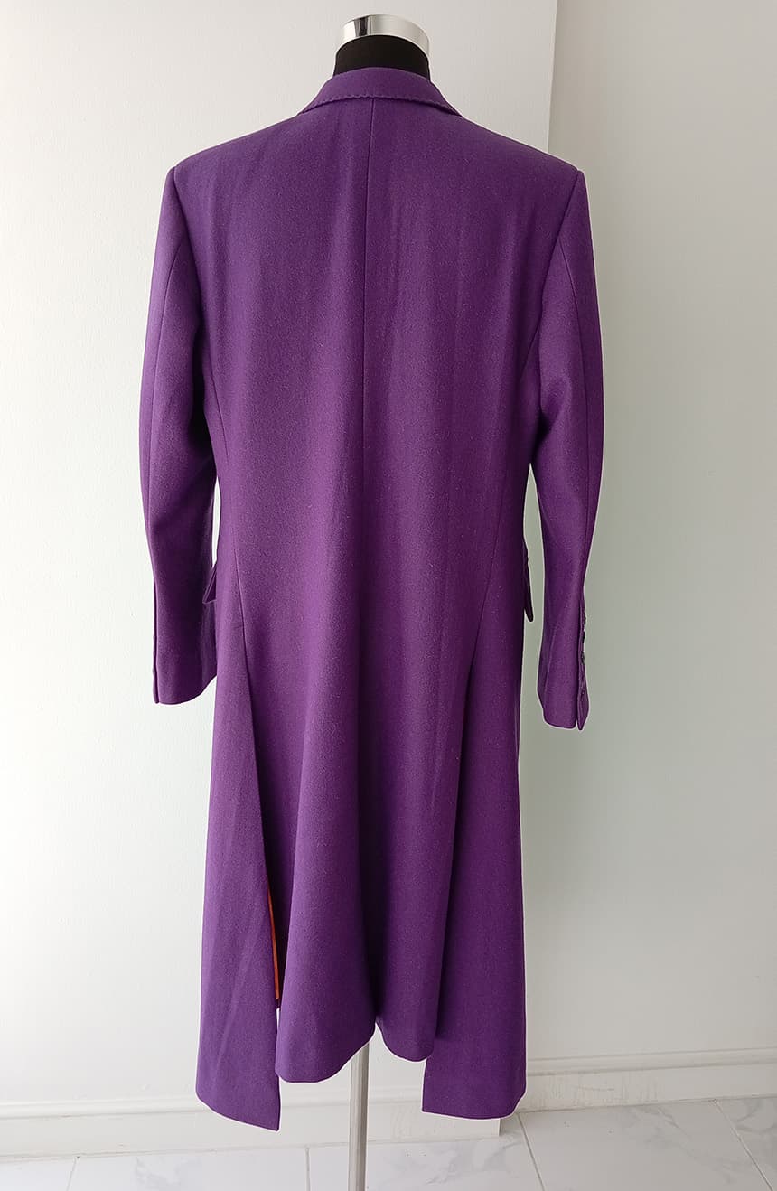 Rear view of a Heath Ledger Joker inspired purple coat from The Dark Knight, displayed on a mannequin against a white background. This tailored long purple overcoat features structured shoulders, a fitted silhouette, dramatic asymmetric hem, and signature villain-inspired styling influenced by the iconic Joker costume design from the film.