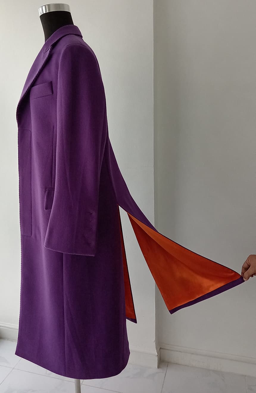 Detailed view of the asymmetric flowing hemline on a Heath Ledger Joker inspired purple long coat from The Dark Knight displayed on a mannequin, emphasizing the theatrical silhouette with cosplay-inspired design, and orange lining.
