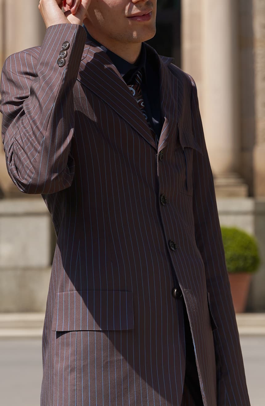 Close-up of 10th brown blue-pinstripe suit jacket with notch lapels, three-button front and flap pocket, worn outdoors.