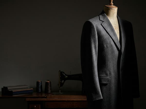 A finished charcoal wool coat on a dress form, lit to show the weave and hand-set sleeve detail.