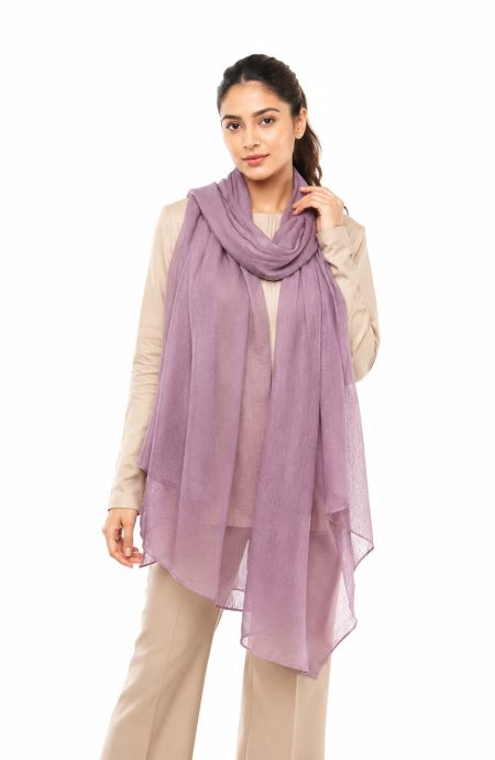 Woman wearing a mauve featherlight cashmere scarf looped once at the neck, the sheer ends hanging to knee length over a cream top and beige tailored trousers.