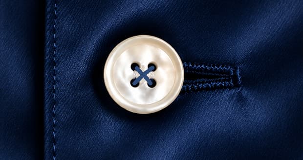 Close-up of a mother-of-pearl button sewn onto a navy silk pajama shirt front.