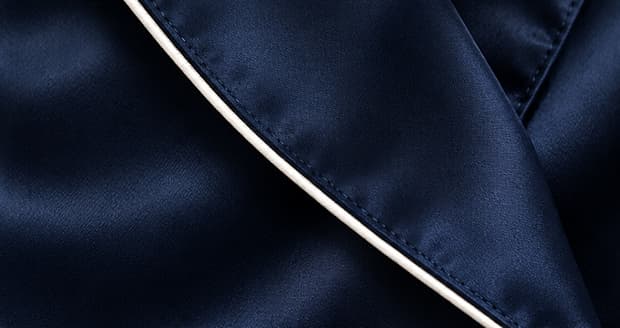 Detail of a navy silk robe's shawl collar edged with a continuous line of ivory corded piping.